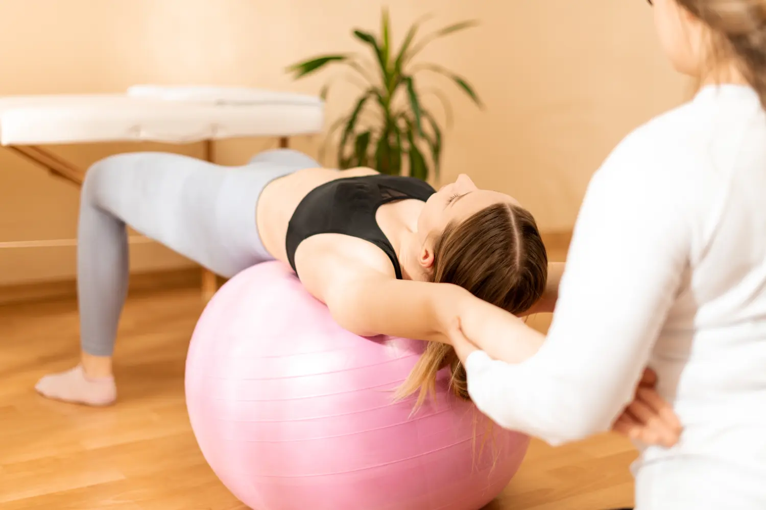 Physiotherapeutin arbeitet mit einer jungen Klientin an der Rumpfmuskulatur mithilfe von Fitball. Hintergrund in Rehabilitation und Physiotherapie.